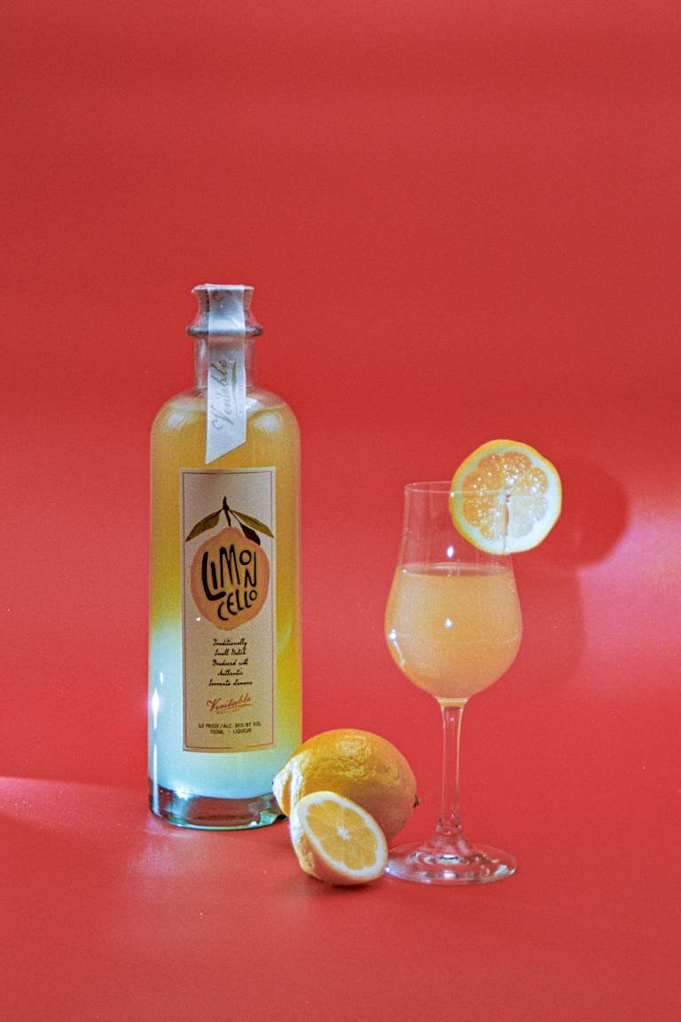 Limoncello bottle and lemon slices on a vibrant red background, evoking refreshing citrus vibes.